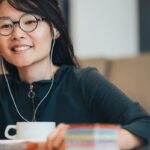 Frau mit Kopfhörern arbeitet lächelnd am Laptop.