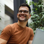 Hombre sonriente con portátil en jardín interior